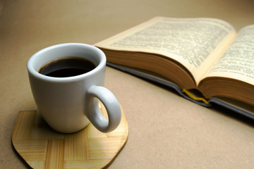 White cup with coffee on a wooden stand with a book on a beige background