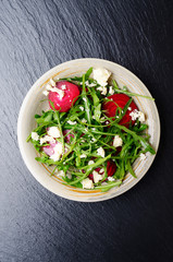 Top view at clay dish with beetroot arugula and feta cheese salad on slate stone tray closeup view
