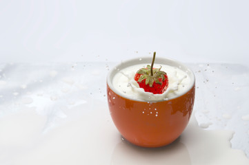 Strawberries fell into the milk in an orange glass until the milk spread beautifully on a white background.