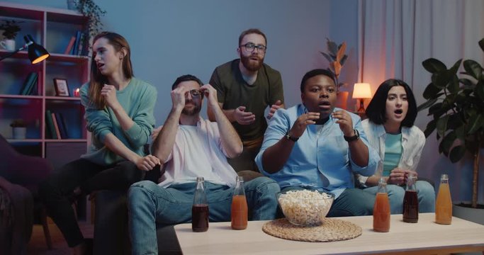 Emotional male and female friends sitting near tv looking exited and than become upset. Group of people sitting on sofa ant supporting sport team. Concept of entertainment.