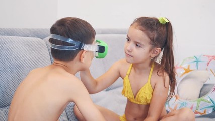Boy and girl wearing swimming suits are sitting is a sofa. Girl is cheching wether boy sees something. Close up. Copy space. 4K.