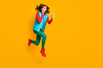 Fototapeta na wymiar Full length profile side photo astonished girl jump use smartphone read unbelievable social network information run wear red blue green vest pants boots isolated bright shine color background