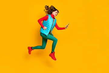 Fototapeta na wymiar Full size profile side photo cheerful girl student jump use smartphone follow social media ads run hurry wear blue vest red green pants trousers shoes isolated bright yellow color background