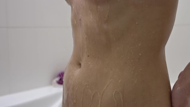 Water running down the belly of a young naked woman taking a shower.