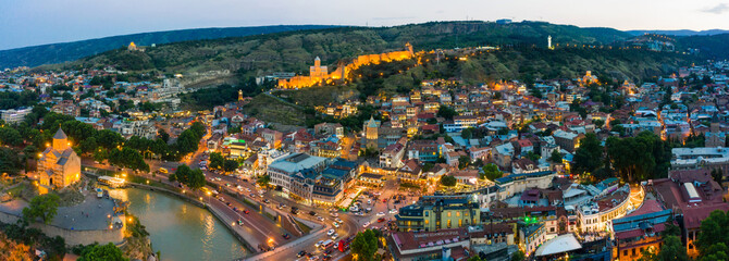 The evening panorama of the old town on Sololaki hill, crowned with Narikala fortress, the Kura river reflects the evening city lights and cars traffic with blure in Tbilisi, Georgia © miklyxa