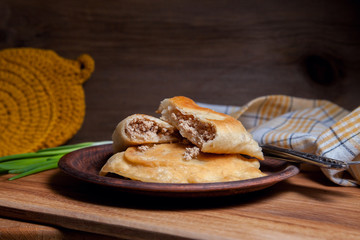 Clay plate of fried meat pies with cutlery and green onion on wooden table.