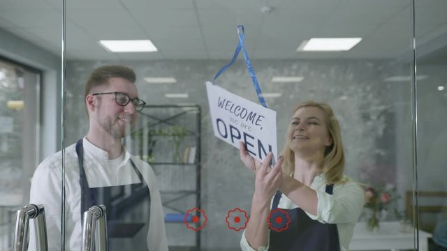 male and female entrepreneurs small business owners change name from CLOSED to OPEN, smile look at camera and point fingers at it, successful startup