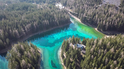 A drone shot of anAlpine valley in Austria. The valley has a Green Lake in the middle.  A headland in the middle of the lake. The algae give the lake distinctive color. Early spring in the mountains