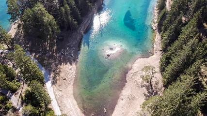 A drone shot of anAlpine valley in Austria. The valley has a Green Lake in the middle.  A headland in the middle of the lake. The algae give the lake distinctive color. Early spring in the mountains