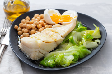 fried cod fish with chick pea, boiled egg and cabbage on dark dish