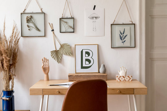 Design scandinavian interior of home office space with a lot of mock up photo frames, wooden desk, brown chair, flowers, office and personal accessories. Stylish neutral home staging. Template.