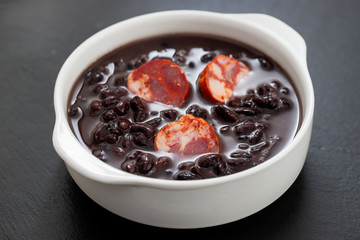 typical brazilian food black beans with smoked sausages in white bowl
