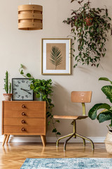 Retro interior design of living room with design vintage chair and commode, plants, cacti, clock, personal accessories and gold mock up poster frame on the beige wall. Stylish home decor. Template. 