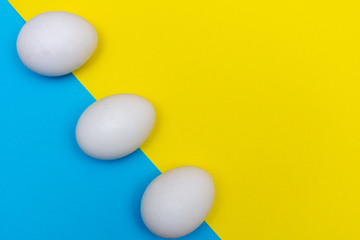 Three Easter holiday flat lay with white egg on a solid bright blue and yellow vibrant background with copy space.