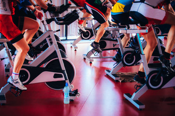 Spinning class, group activity on stationary bike. Team cardio excercise on bicycle. - obrazy, fototapety, plakaty