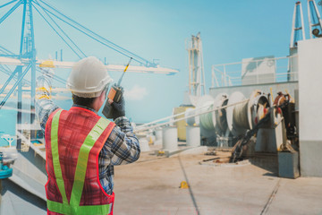 Fototapeta premium Engineer, Pilot captain with walkies talkie in hand on vessel forward ship with anchor rope in drum and crane in port background