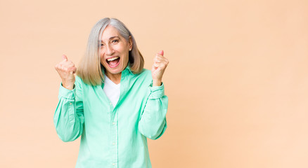 middle age cool woman feeling happy, positive and successful, celebrating victory, achievements or...