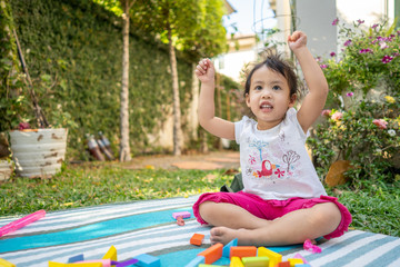 Cute little girl sitting in garden playing with wooden building blocks