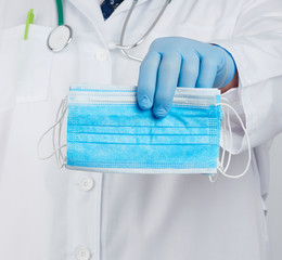 doctor in a white coat, blue latex sterile gloves holds textile medical masks