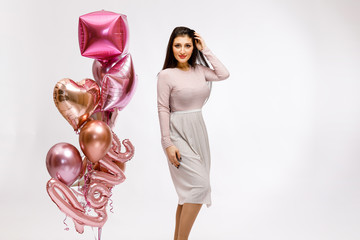 A young beautiful brunette girl in a powder dress has a fun for Valentine's day, hen party or baby shower on a white background with bright helium balloons