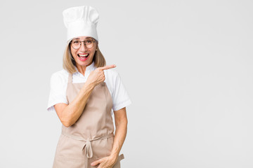 middle age baker woman looking excited and surprised pointing to the side and upwards to copy space...