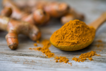 Turmeric powder and fresh turmeric in wood bowls on wooden table.