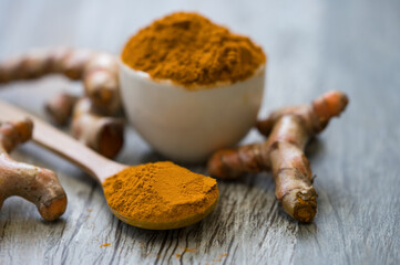 Turmeric powder and fresh turmeric in wood bowls on wooden table.