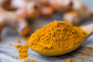 Turmeric powder and fresh turmeric in wood bowls on wooden table.