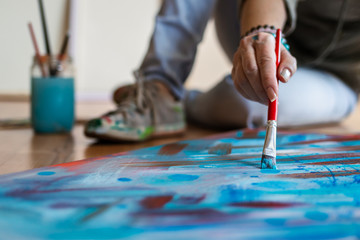 Woman painting modern abstract paintings at studio. Selective focus on paintbrush and canvas