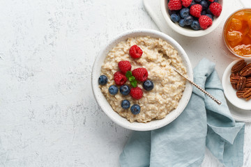 Oatmeal rustic porridge with blueberry, raspberries, jam and nuts in white bowl, dash diet