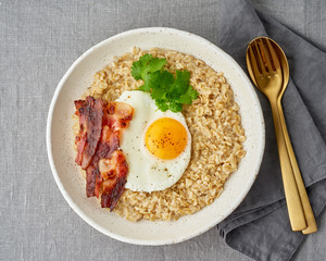 Oatmeal, fried egg and fried bacon. Hearty fat high-calorie breakfast, source of energy.