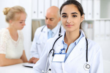 Fototapeta premium Doctor woman in clinic with colleagues at the background. Hispanic or latin american staff in medicine