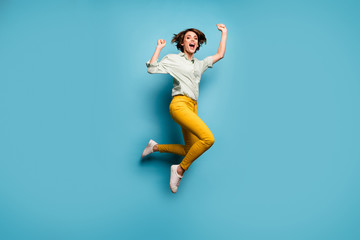 Fototapeta na wymiar Full size photo of funky lady jumping high up celebrating weekend vacation start beginning wear casual green shirt yellow pants shoes isolated blue color background