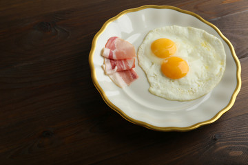 fried eggs served with bacon on a luxury plate on a wooden background