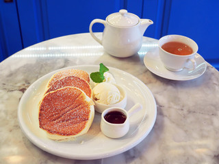 Homemade fluffy souffle pancake, topped with sugar icing, served with maple syrup, whipped cream and vanilla ice cream. Tea time concept.