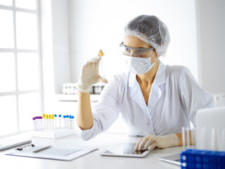 Professional female scientist in protective eyeglasses researching tube with reagents in...