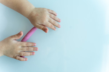 Little children's handles roll a sausage made of pink mass for modeling on a light surface. children's creativity