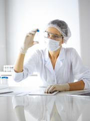 Professional female scientist in protective eyeglasses researching tube with reagents in laboratory. Concepts of medicine and research