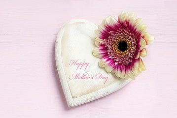 Fototapeta na wymiar white painted wooden heart shape and a flower head on a bright pink background, text Happy Mother's Day, top view from above with copy space