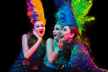 Celebrate. Beautiful young women in carnival, stylish masquerade costume with feathers on black background in neon light. Copyspace for ad. Holidays celebration, dancing, fashion. Festive time, party.
