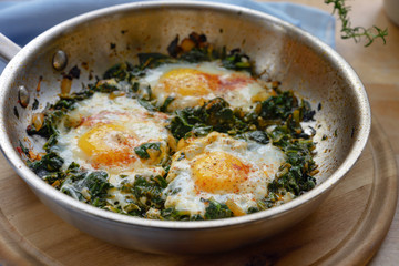 cooking pan with spinach and fried eggs, spices and herb garnish, healthy dish for low carb diet on...