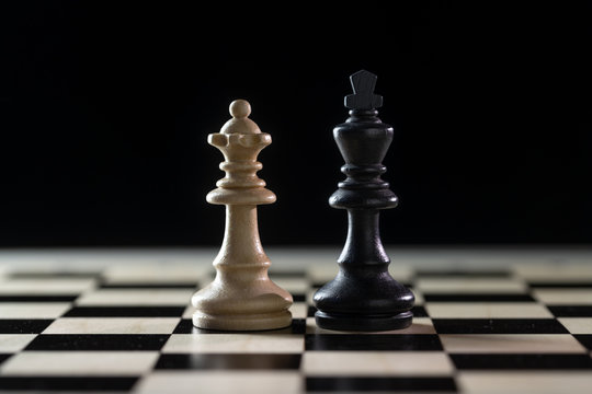 Two chess pieces, white queen and black king side by side on a chessboard against a dark background, concept for diversity, gender equality and cooperation, copy space