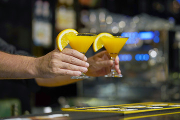 Hand of bartender gives two orange cocktail. Alcoholic, non-alcoholic drink-beverage at the bar counter in the night club. Two orange cocktail. Evening time. The concept of service.