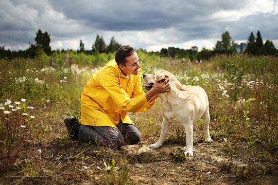 Guy In Yellow Jacket Kissing Lovely Big Dog During Walk In Filed