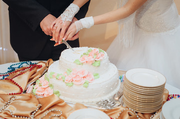 The bride and groom, holding hands, cut a delicious and decorated wedding cake with a knife close-up. Wedding dessert. Photography, concept.