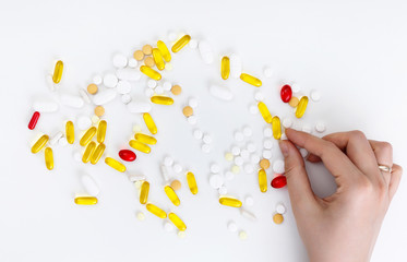 Female hands hold multi-colored pills on a white background. Top view. Health concept.