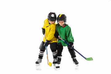 Little hockey players with the sticks on ice court and white studio background. Sportsboys wearing equipment and helmet practicing. Concept of sport, healthy lifestyle, motion, movement, action.