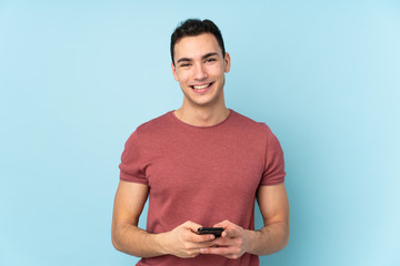 Young caucasian handsome man isolated on blue background sending a message with the mobile