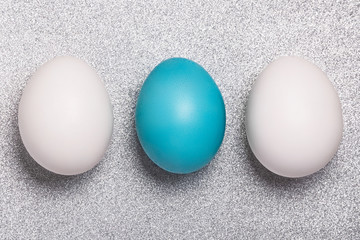 Big easter blue egg with two white egg on a shine silver background. Concept for greeting card.