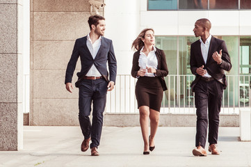 Cheerful successful coworkers talking on their way to office. Business people walking outdoors and chatting. Friendly officemates concept